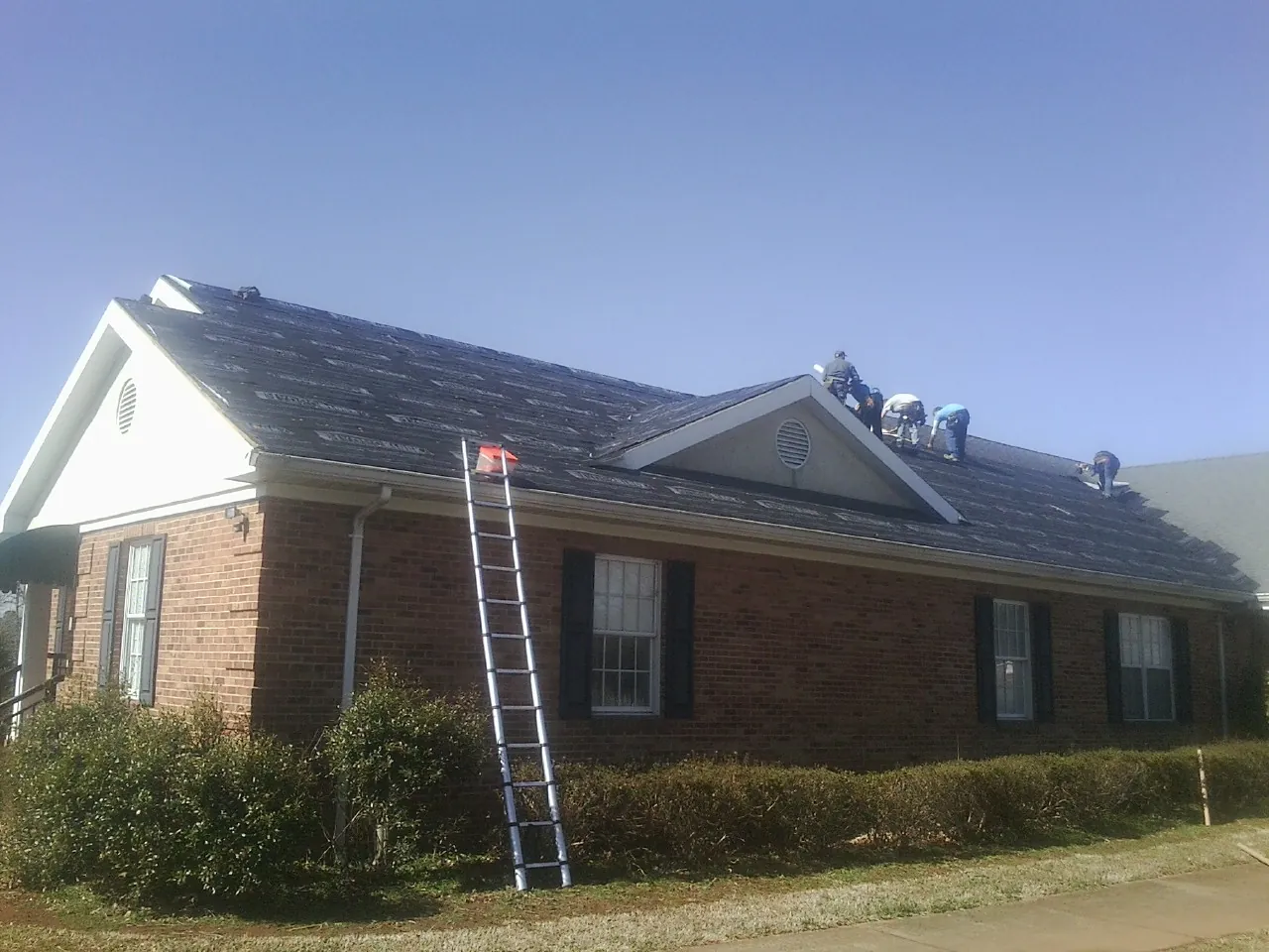 Crew tearing shingles off a brick ranch roof with a ladder set — Emergency Roof Repair work by our crew in New Providence