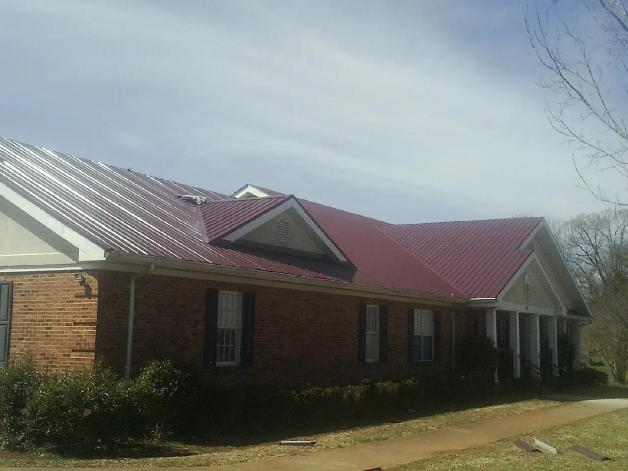 Red metal roof with gabled entries on a long brick building, from a Hail Damage Roof Repair job in New Providence