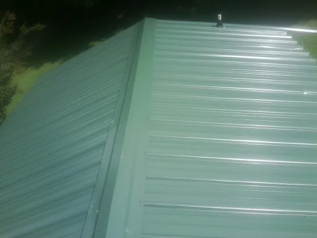 New green metal panels meeting at the ridge of a roof — Flat Roof Repair work by our crew in New Providence
