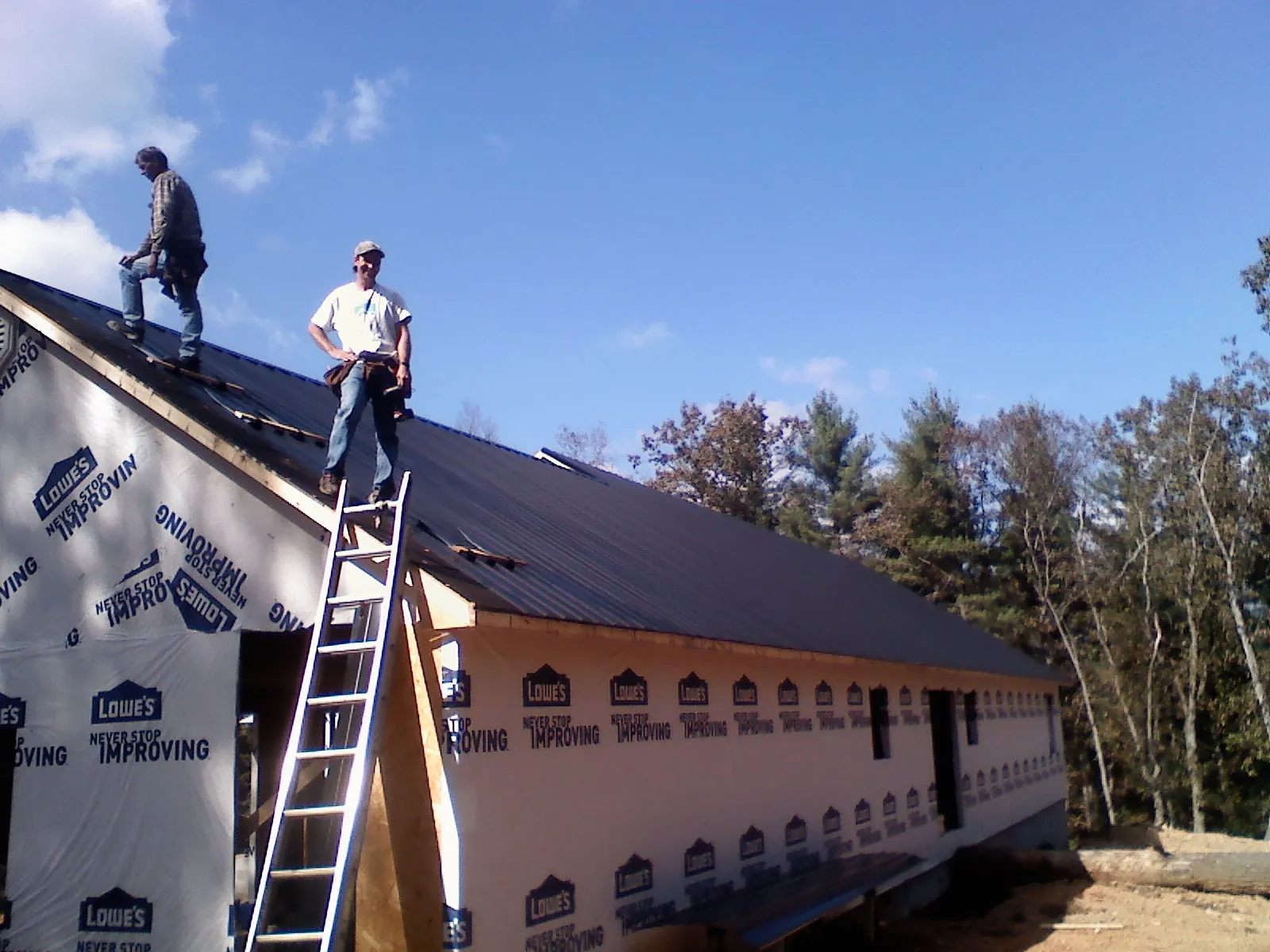 Two roofers standing on a long dark metal roof over a wrapped building in New Providence